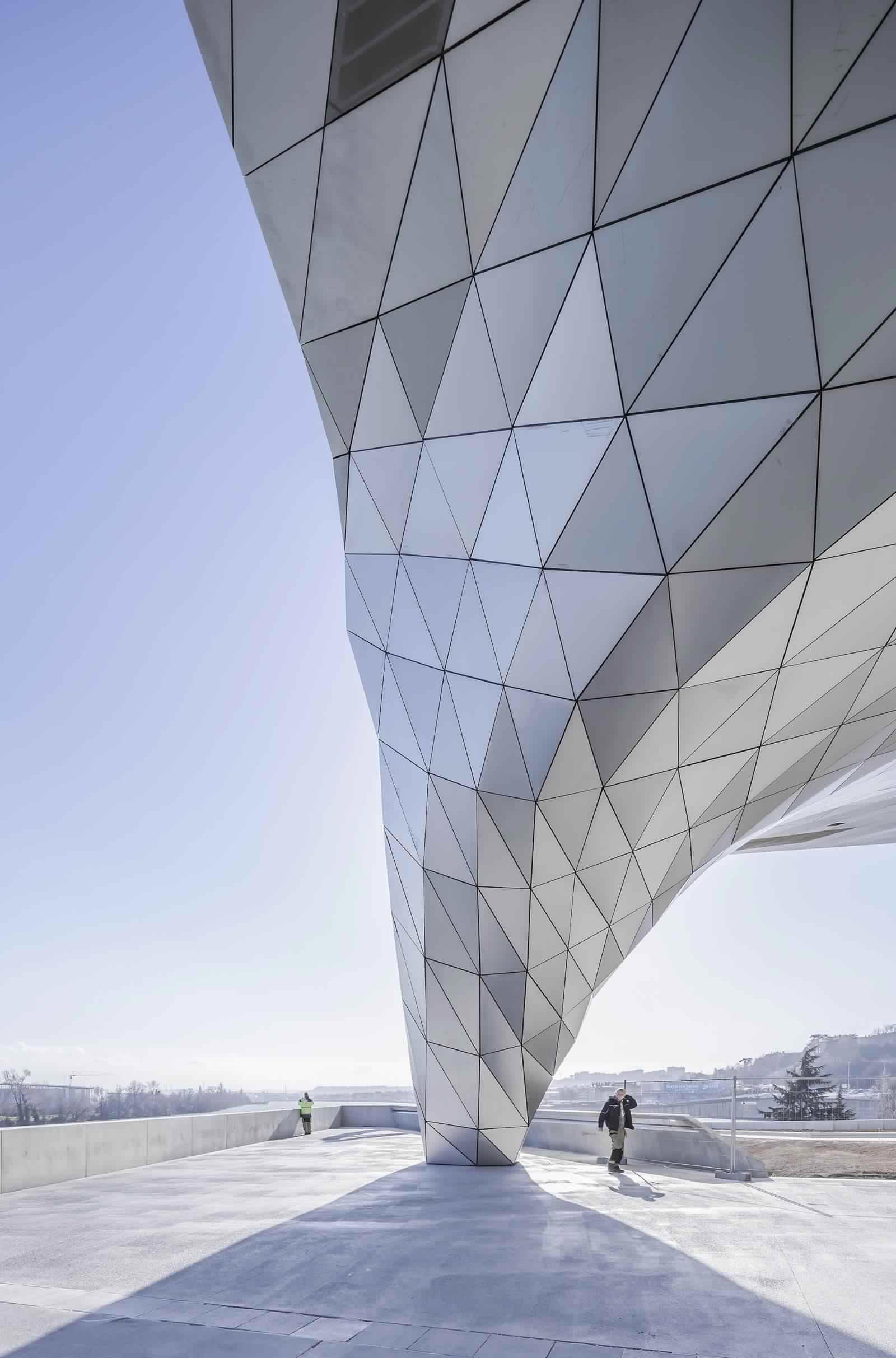 edificio desde el exterior con una gran vista a la ciudad y la presencia de dos personas visitando el Museo Musée des Confluences